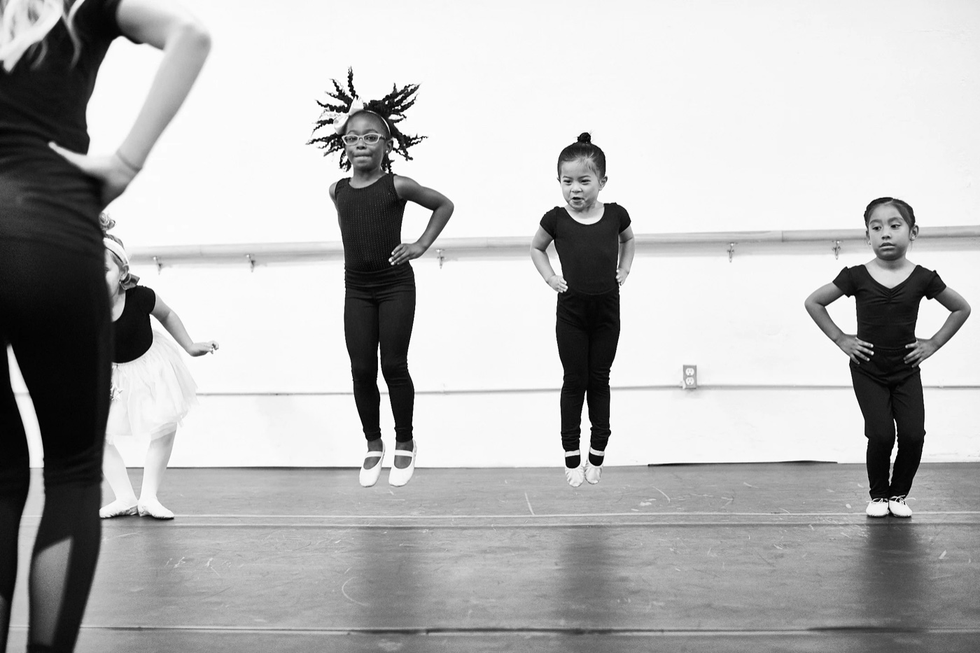 Three young dancers jumping in unison during a class, teacher watching